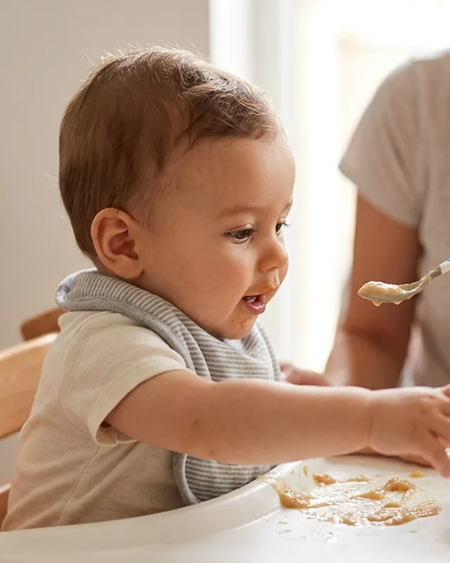 A baby reaching for food and watching an adult eat